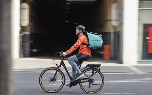 Delivery man wearing a bicycle helmet and food delivery bag | Gannes & Musico, LLP