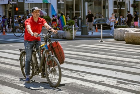 Man in a red shirt from a delivery service on a electrical bike in a zebra crossing in NYC