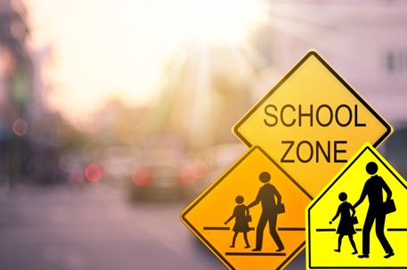 School zone warning sign on blur traffic road with colorful bokeh light abstract background.