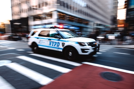 An NYPD police car driving through a New York City intersection. | Gannes & Musico, LLP
