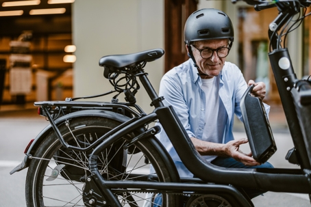 A man wearing a helmet adjusting the battery on an electric bicycle. | Gannes & Musico, LLP
